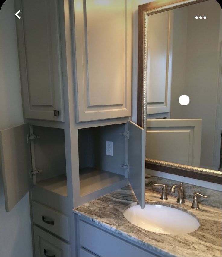 a bathroom vanity with marble counter top and white cabinetry, mirror above the sink