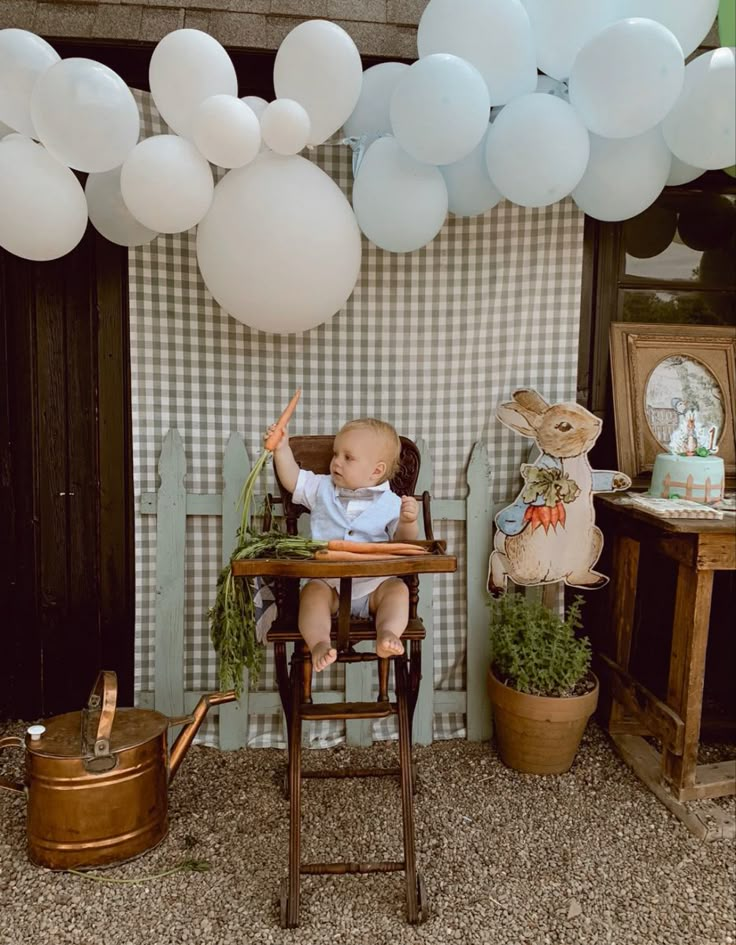 a baby sitting in a highchair with balloons and decorations on the wall behind him