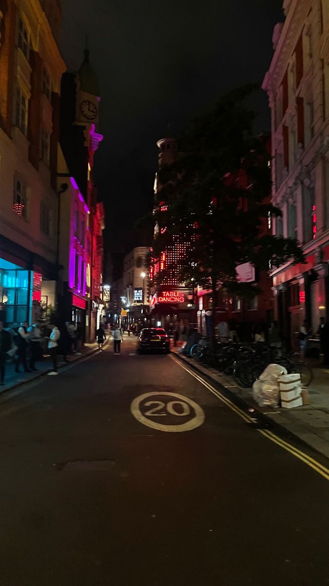 an empty city street at night with people walking on the sidewalk