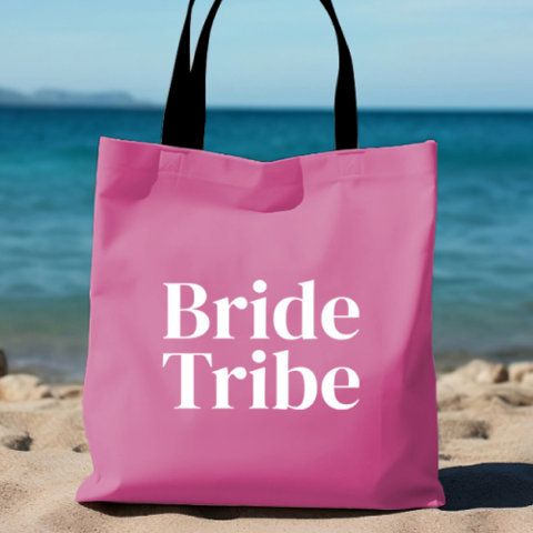 a pink tote bag with the words bride tribe on it sitting in the sand