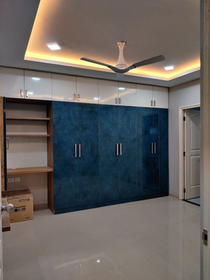 an empty room with blue and white cupboards on the wall, and a ceiling fan