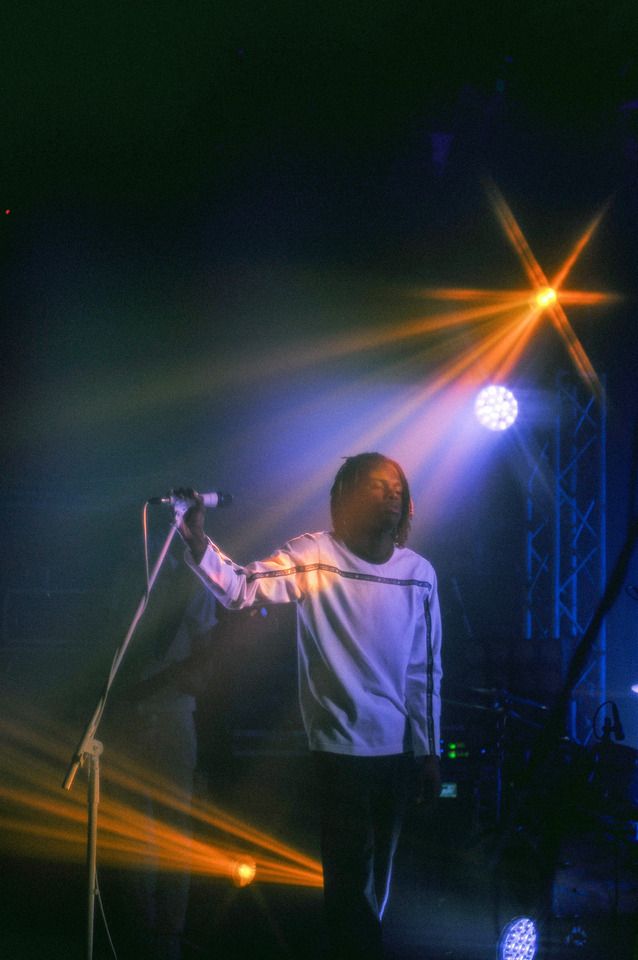 a man standing in front of a microphone on top of a stage with lights behind him