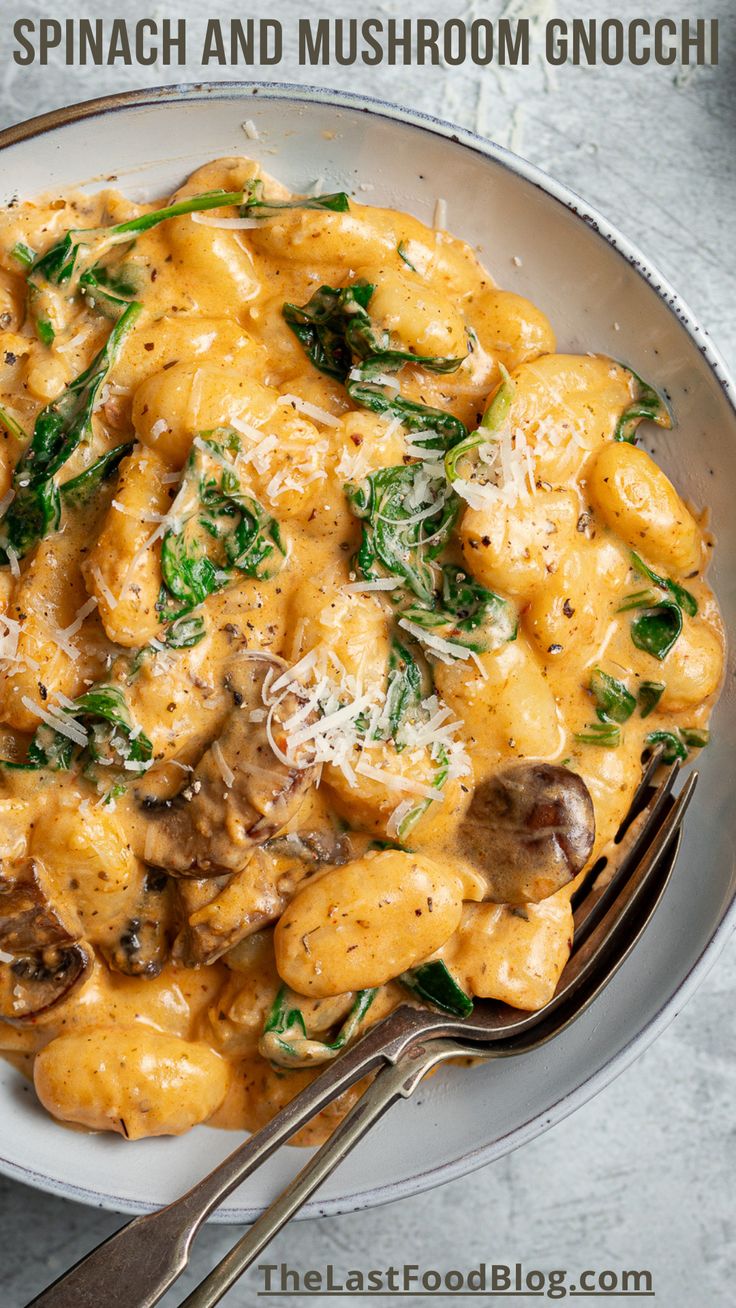 a bowl filled with pasta and spinach on top of a white plate next to a fork