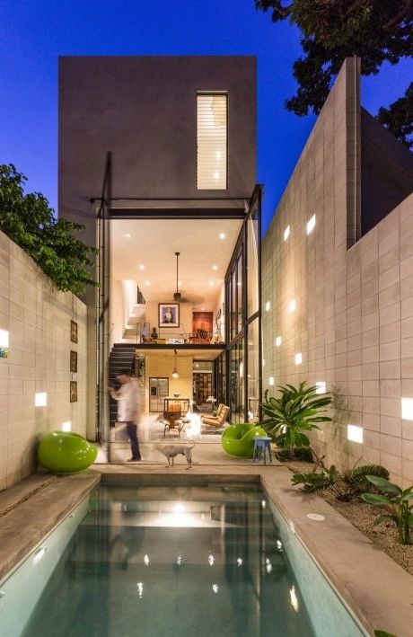 an indoor swimming pool in the middle of a backyard with lights on and people walking around