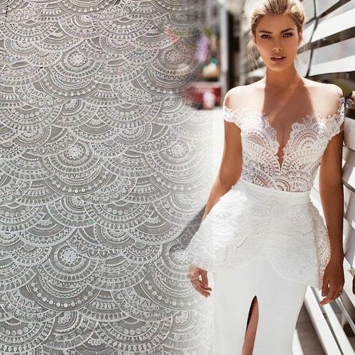 a woman in a white dress standing next to a wall with an intricate design on it