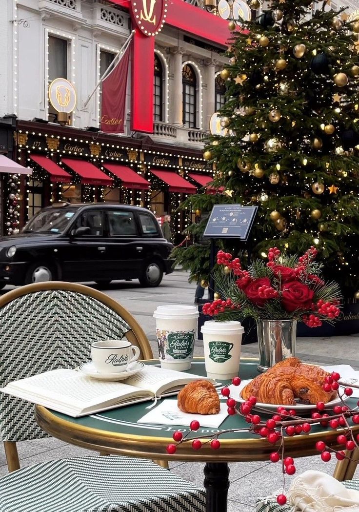 a table topped with croissants and coffee next to a christmas tree in front of a building