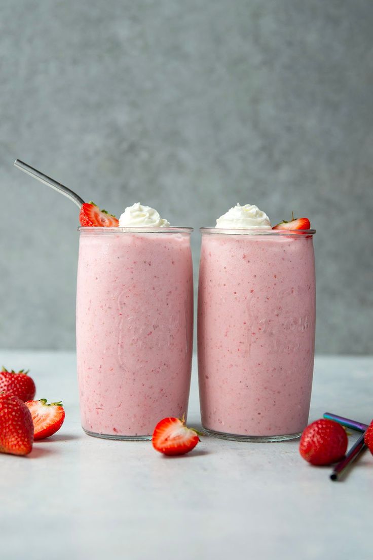 two strawberry milkshakes with whipped cream and strawberries