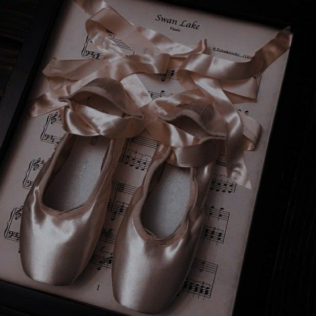 two pairs of ballet shoes sitting on top of sheet music with ribbon tied around them