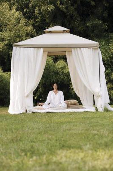 a woman sitting in the middle of a lawn under a gazebo with white drapes