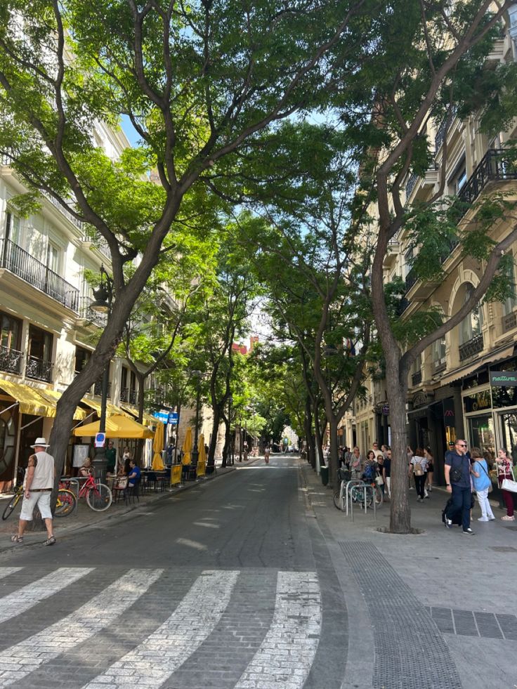 people are walking down the street in front of buildings and trees with yellow umbrellas