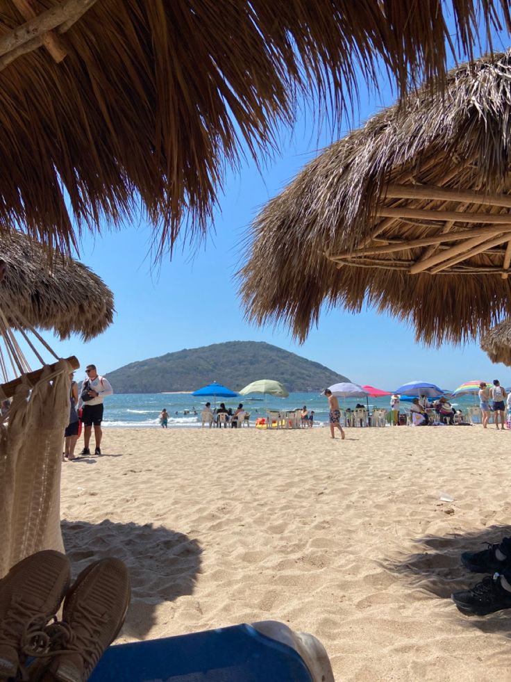 people on the beach under straw umbrellas and chairs with their feet in the sand