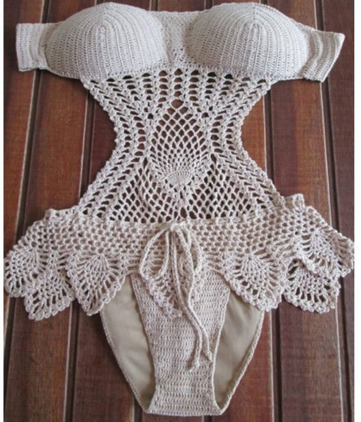 a crocheted bodysuit is laying on top of a wooden floor with white lace