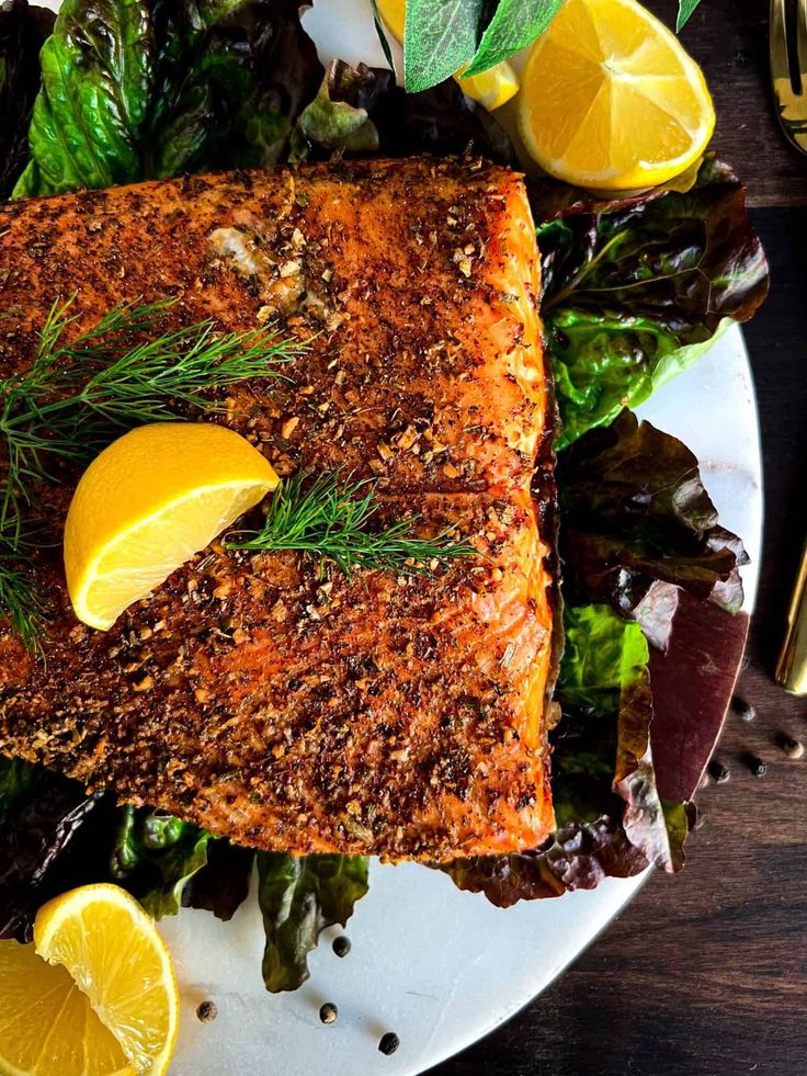 a white plate topped with fish next to lemon wedges and lettuce covered in seasoning