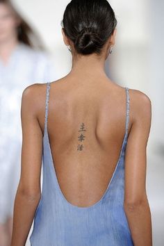 a woman with a tattoo on her back walking down the runway at a fashion show