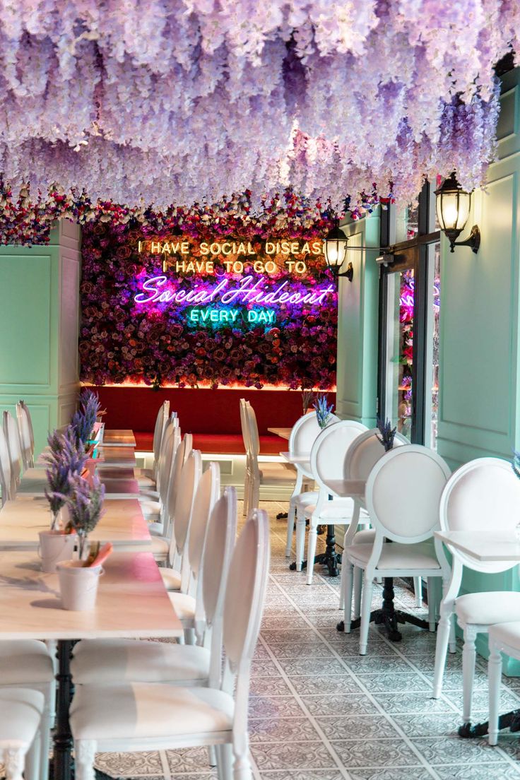 tables and chairs are lined up with purple flowers hanging from the ceiling in front of them