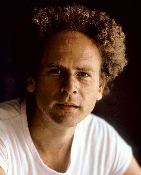 a man with curly hair wearing a white t - shirt and looking at the camera