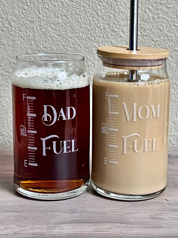 two beer mugs sitting next to each other on top of a wooden table with a straw in it