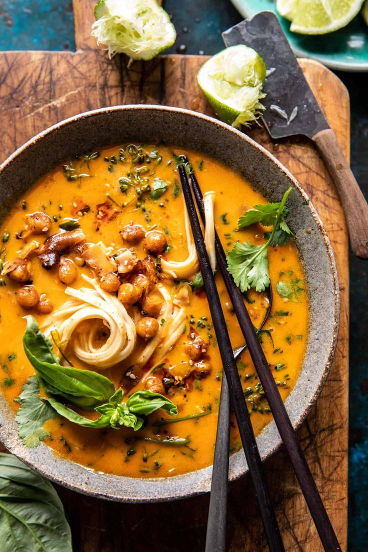 a bowl of soup with noodles and garnishes on a wooden cutting board