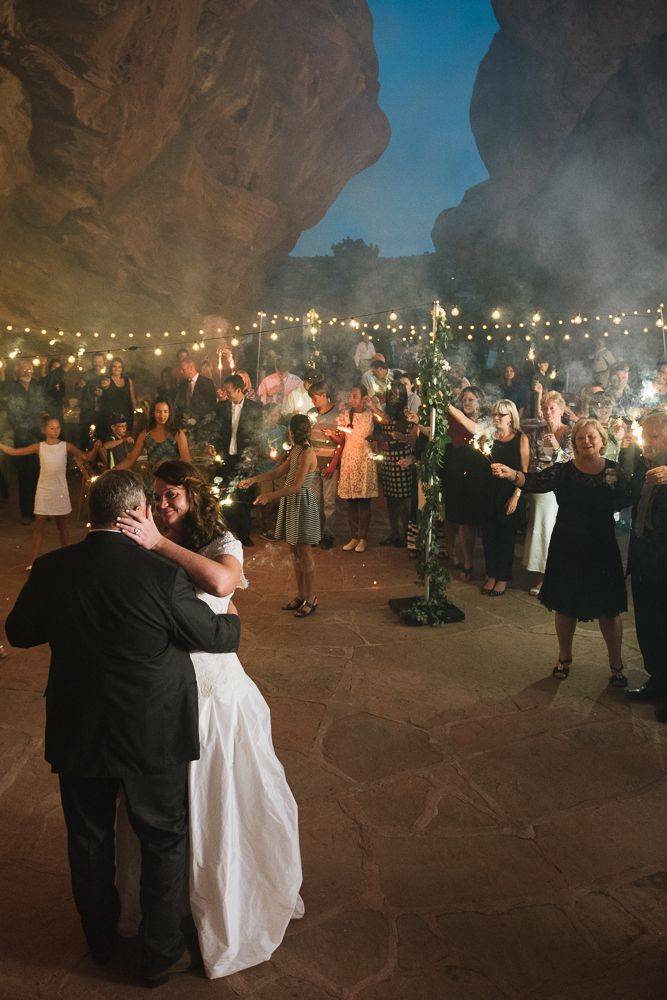 a bride and groom hug in front of their guests as they dance with sparklers