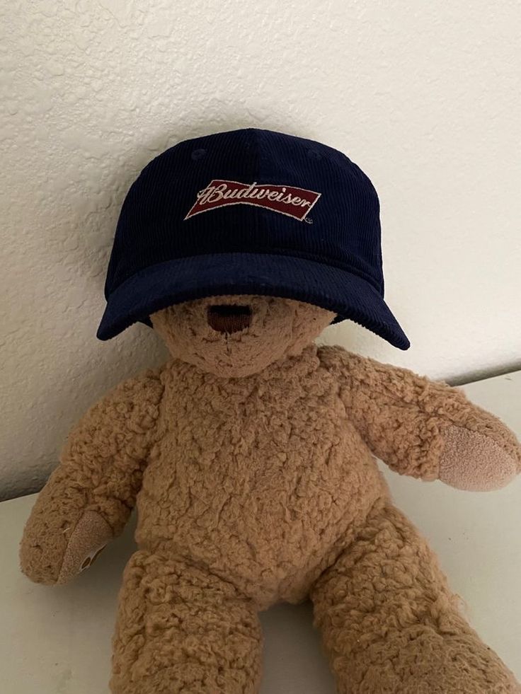 a brown teddy bear with a blue hat on it's head sitting against a white wall