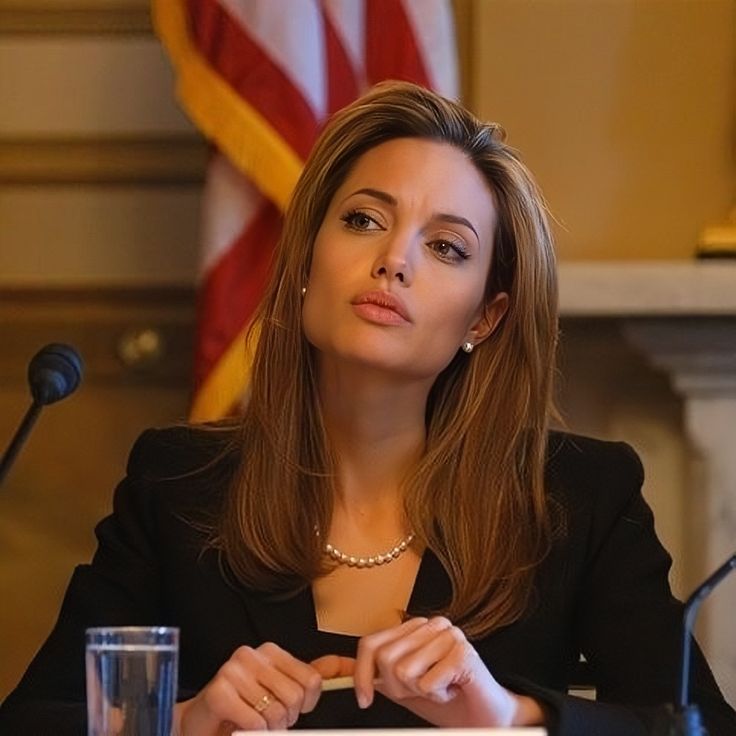 a woman sitting at a table in front of a microphone with an american flag behind her