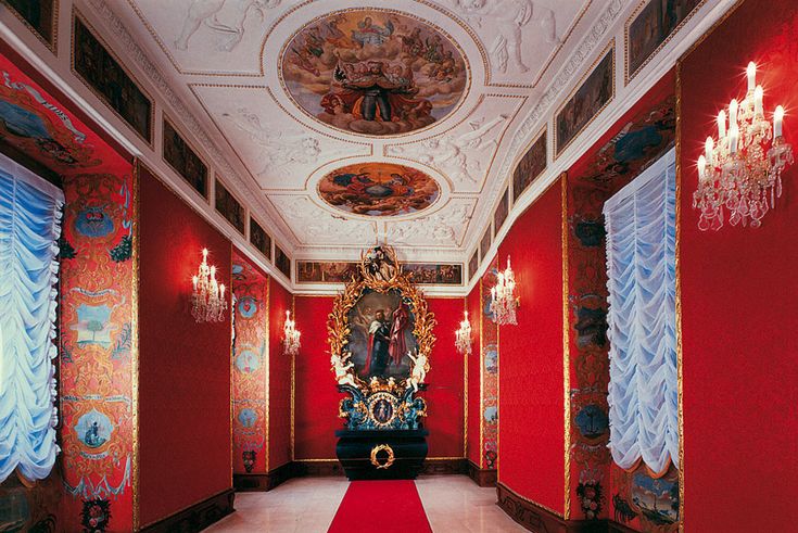 an ornate hallway with red walls and paintings on the ceiling, chandelier and carpet