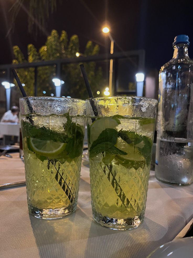 two glasses filled with lemonade and mint on top of a table