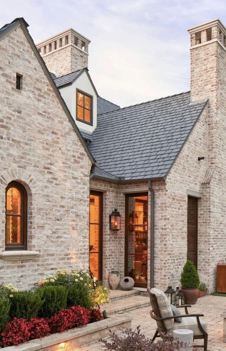 a brick house with an outdoor seating area and fire pit in the front yard at dusk