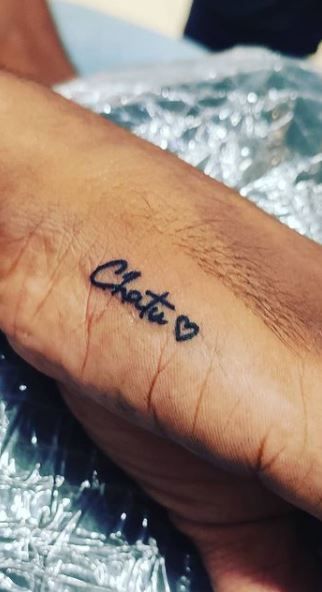 a person with a small tattoo on their left arm and the word chaos written in cursive ink