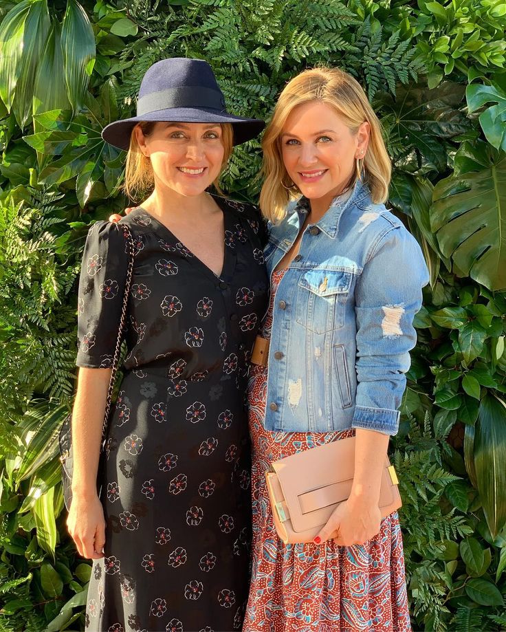 two women standing next to each other in front of green plants and trees with hats on