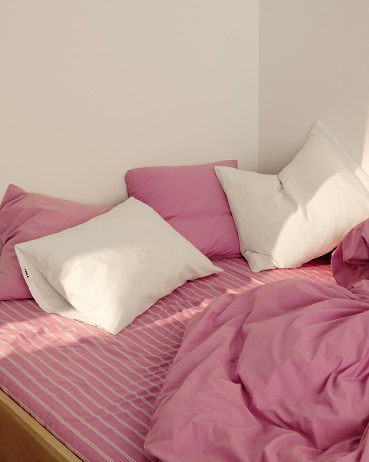 an unmade bed with pink sheets and white pillows