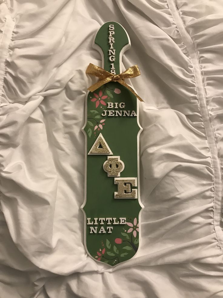 a green and gold tie with letters on it sitting on a white bed spreader