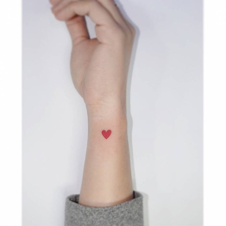 a woman's arm with a small red heart tattoo on her left wrist,