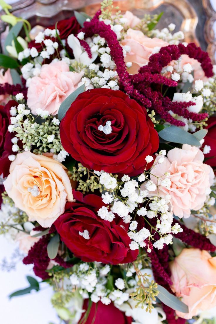 a bouquet of red and pink flowers sitting on top of a silver platter with greenery