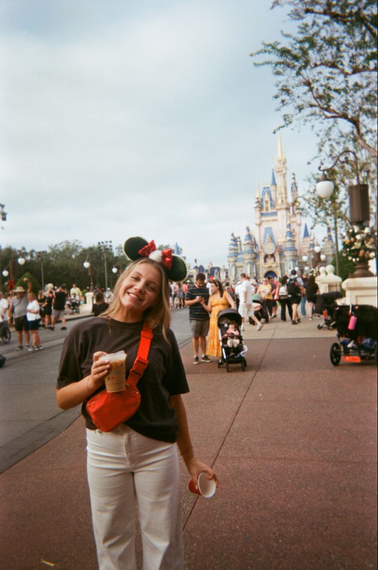 a woman is standing in front of the castle at disney world holding a cup of coffee