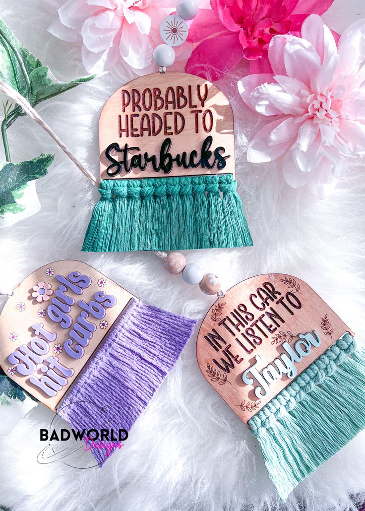 two tassels with words on them sitting next to pink and purple flowers in the background