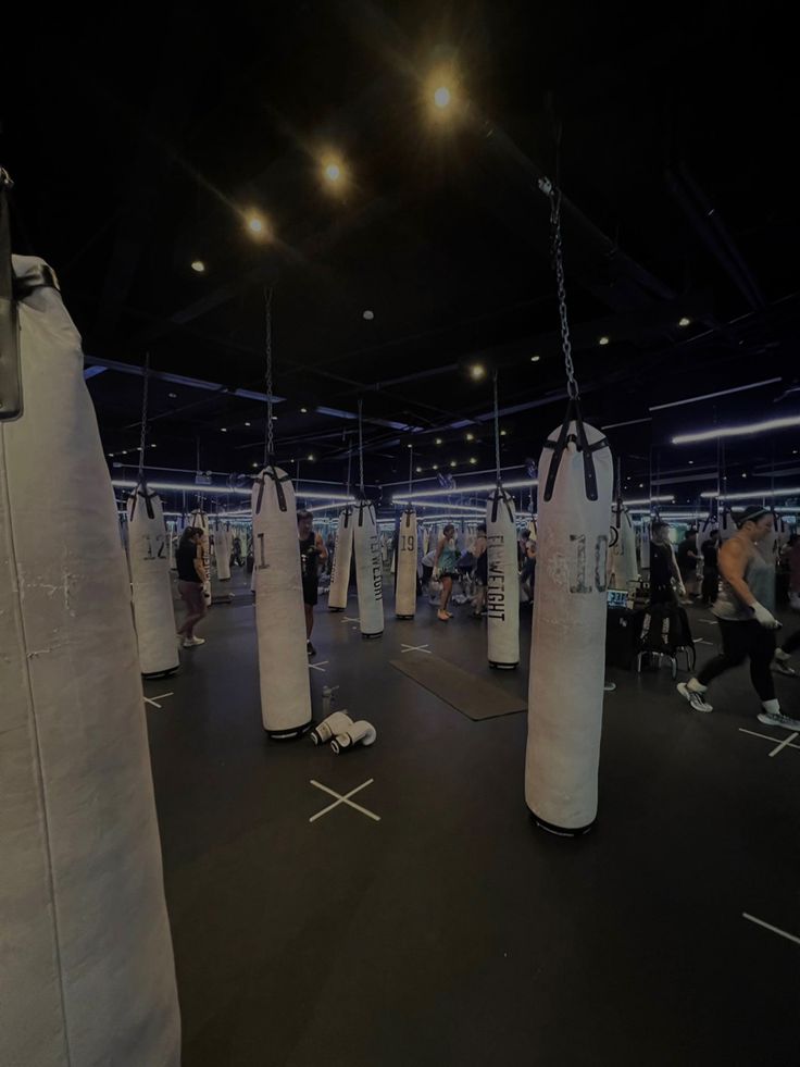 a gym filled with punching bags and people on the sidelines in the dark room