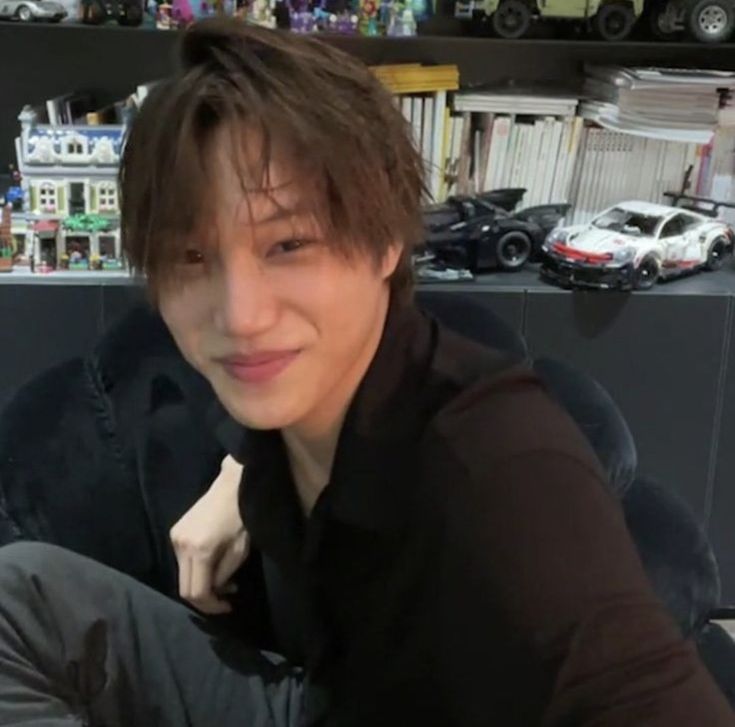 a young man sitting on top of a couch in front of a book shelf filled with toy cars