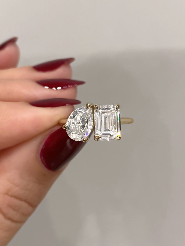 a woman's hand holding an engagement ring with two diamonds on it and red nails