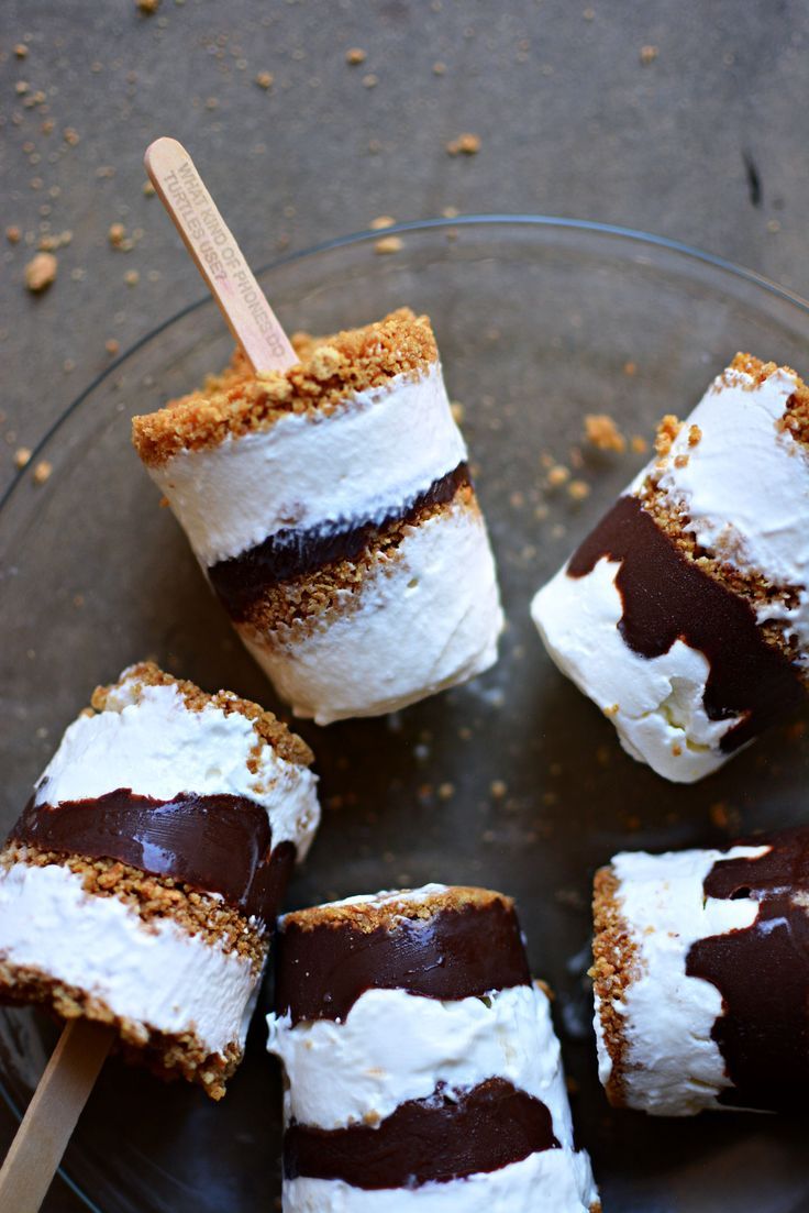 chocolate dipped marshmallows are arranged on a glass plate with wooden skewers