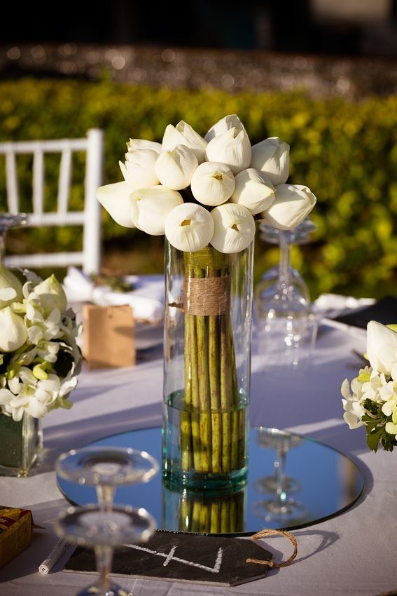 white flowers are in a tall vase on a table with wine glasses and napkins