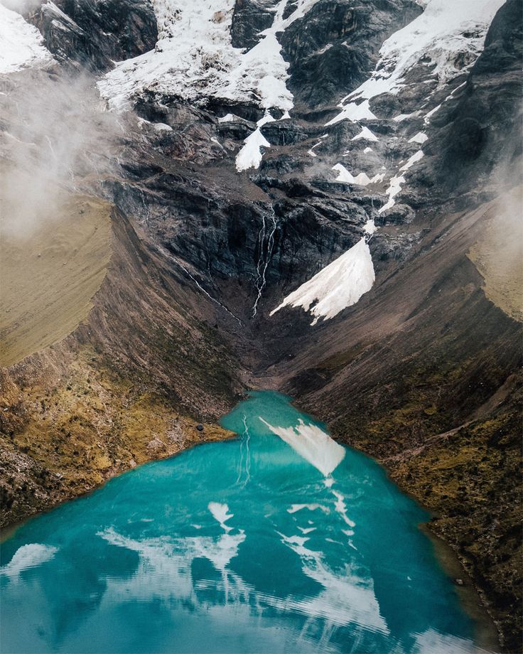 a blue lake surrounded by snow covered mountains in the middle of it's landscape