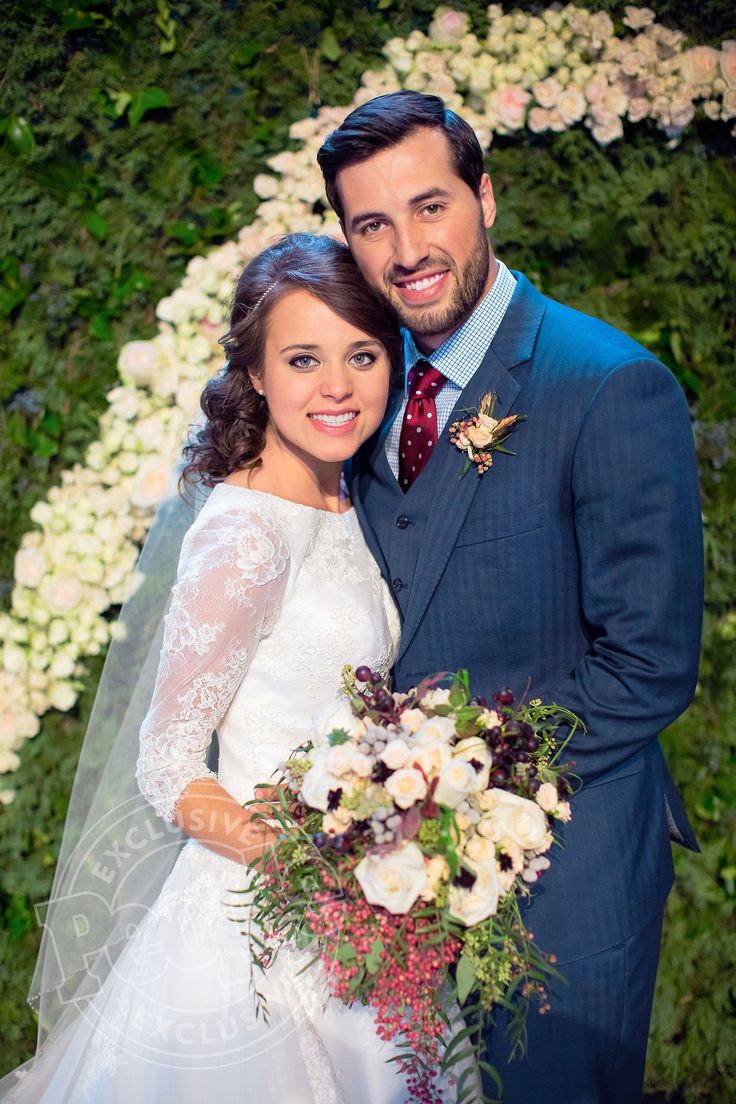 a bride and groom pose for a photo in front of a floral wall at their wedding