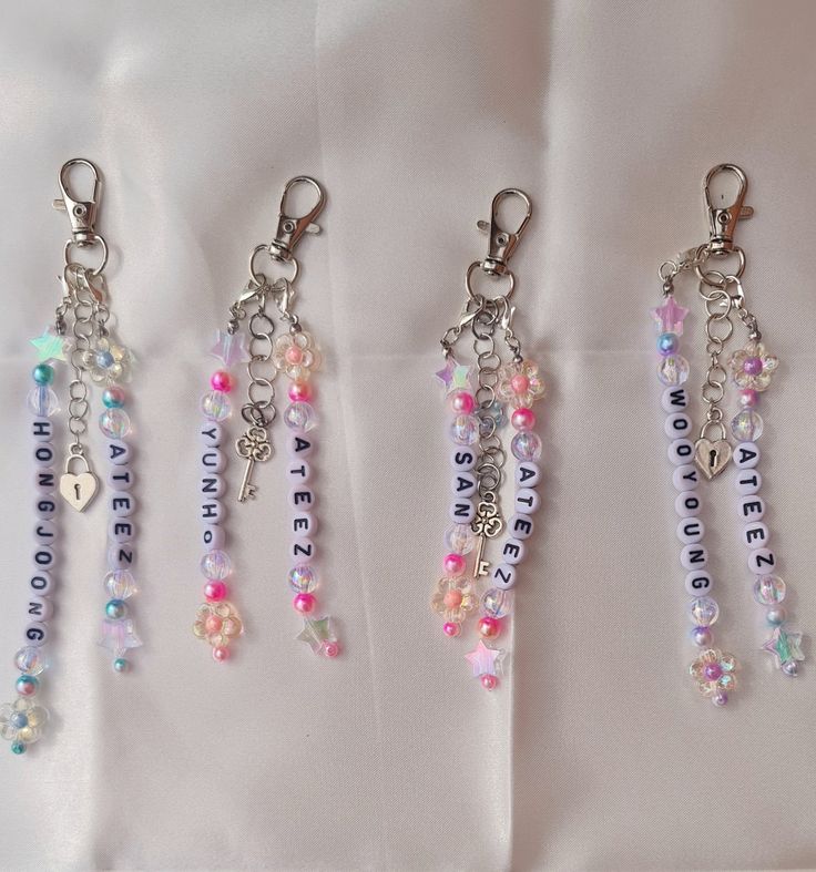 four key chains with charms attached to them on a white cloth covered surface, one has a name tag and the other has several small beads