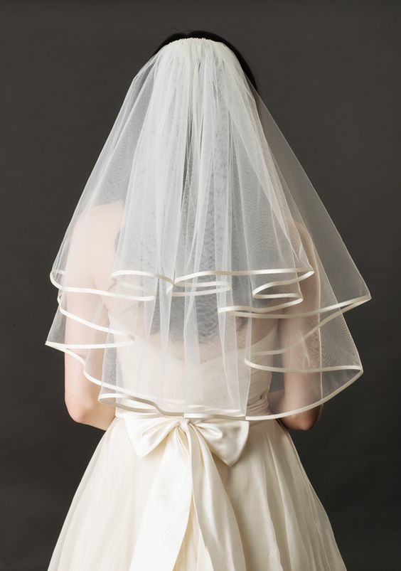 the back of a bride's veil with ribbons on her wedding dress and headpiece