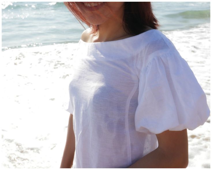 a woman standing on top of a beach next to the ocean with her hair blowing in the wind