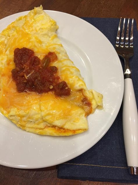 a white plate topped with an omelet covered in cheese and tomato sauce next to a fork