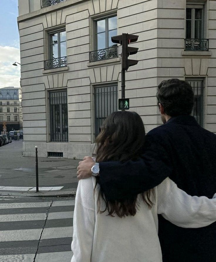 a man and woman walking down the street in front of a tall building with many windows