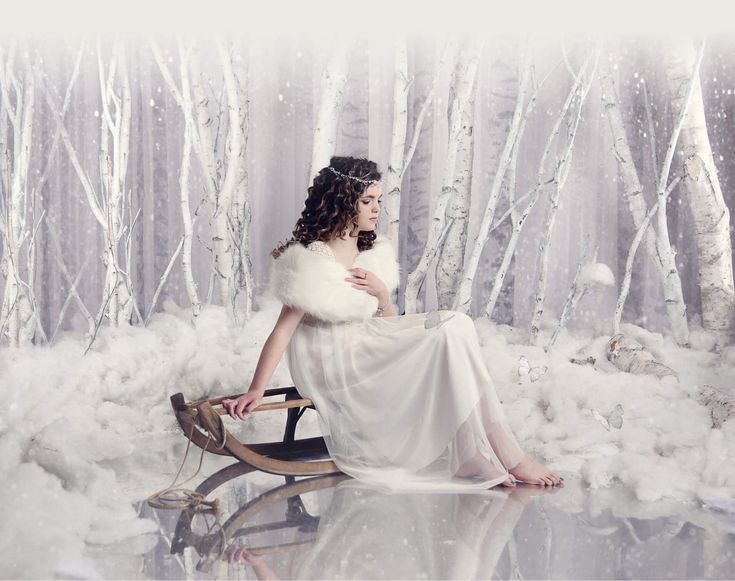 a woman in a white dress and fur stole sitting on a snow - covered bench