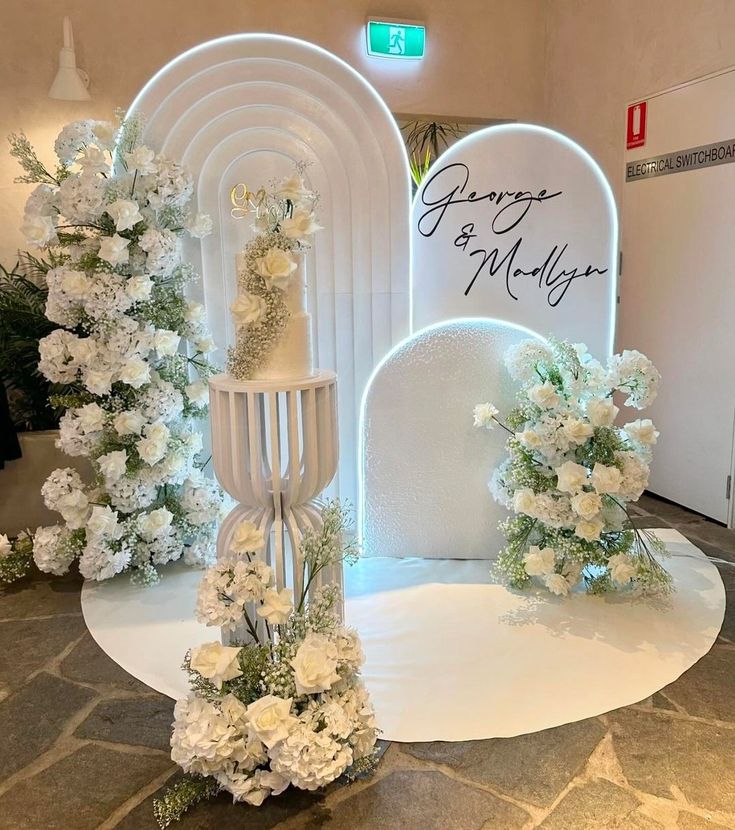 white flowers and greenery on display in front of an arch